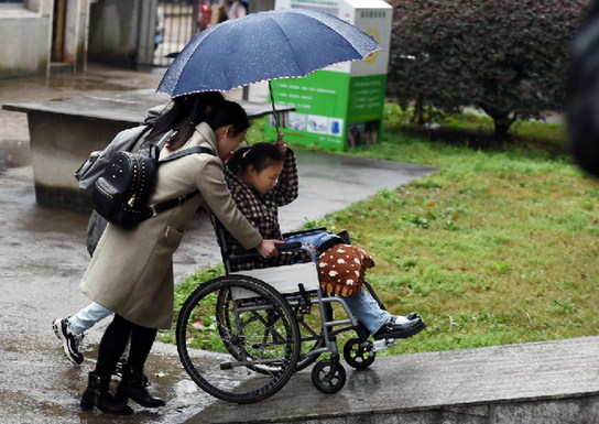 3月9日，下课后两位女生推着轮椅护送陈望回寝室。为方便陈望出入，学校特意安排她和陪读的母亲单独住在宿舍楼一楼离出口最近的一间寝室，并将寝室前的一段阶梯改建成了斜坡。新华社记者 李尕 摄
